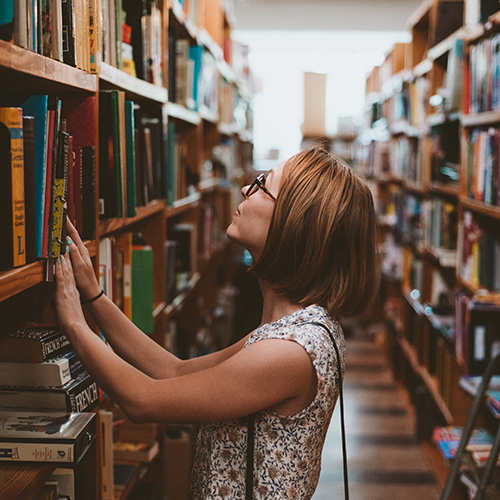 Woman looking at bookshelves in library. Photo by Clay Banks on Unsplash.