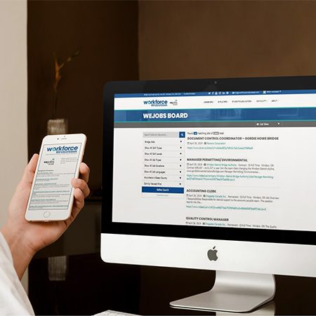 Office professional using WEjobs on a mobile device with large Apple monitor in background, also featuring WEjobs