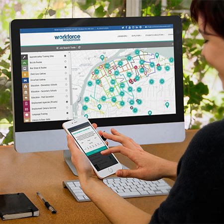 Woman using WEmap jobs board on phone in front of a large monitor featuring Wemap job board